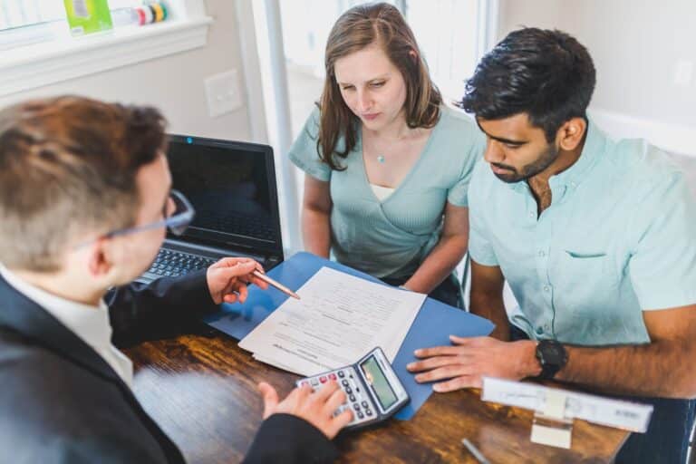 real estate agent in black coat discussing an ownership agreement to a couple inside the office